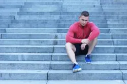 Upset man sitting down in gym clothes regarding Steve Nash Fitness World closing all of its physical locations and terminating all of its employees