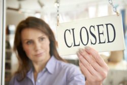 Woman putting up closed sign regarding businesses closing and temporarily laying off thousands of workers amid the COVID-19 pandemic. Lawyers warn the legal risks of temporary layoffs