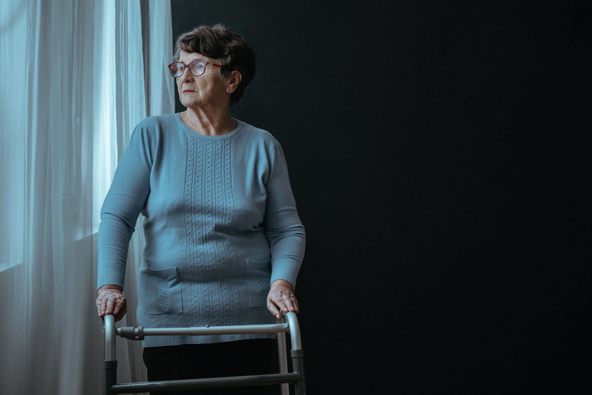 Woman standing in window with walker regarding the nursing home class action lawsuit filed after 31 senior deaths 