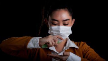 Woman wearing mask and applying hand sanitizer regarding Health Canada issuing a warning to consumers about fraudulent N95 respirators and lifting restrictions on technical-grade ethanol
