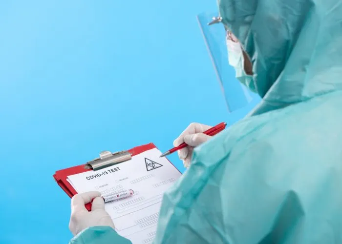 Health worker in hazmat looking at COVID-19 test regarding the false COVID-19 positive results class action lawsuit to be filed