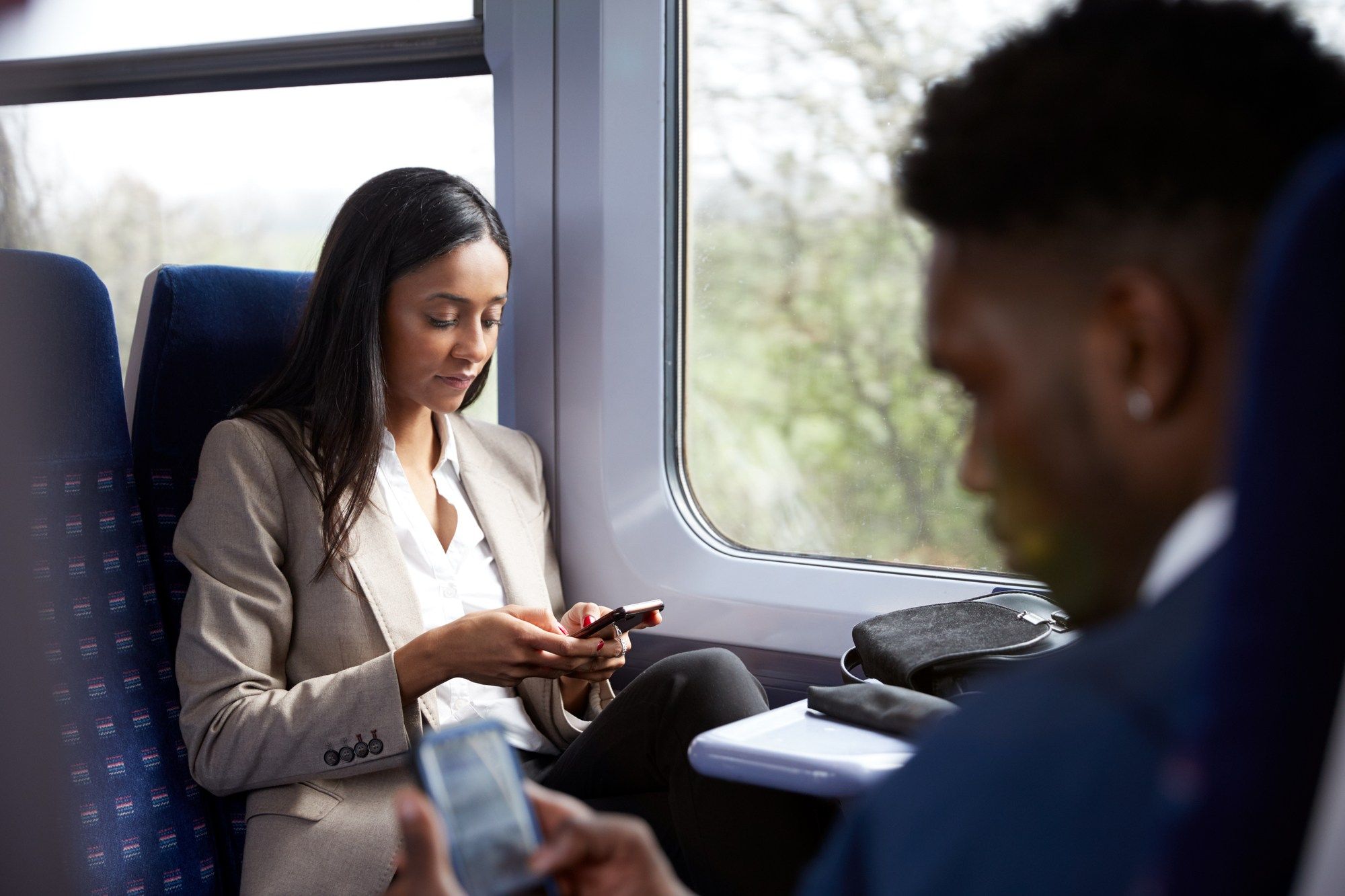 Woman and man looking at their phones on the train regarding information on text spam and how to prevent it 