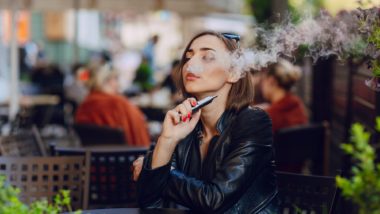 Woman blowing smoke while vaping at table regarding information on whether JUUL e-cigarettes are bad for you