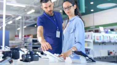 shopper examining electronic device being helped by shop associate regarding product defects