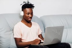 Man using laptop listening to music regarding the Shaw Fibre+ internet lawsuit filed by Telus over misleading advertising 