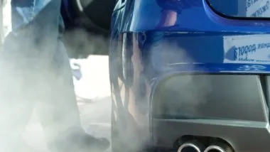 Person standing next to car emitting exhaust regarding the Bosch emissions cheating device class action settlement