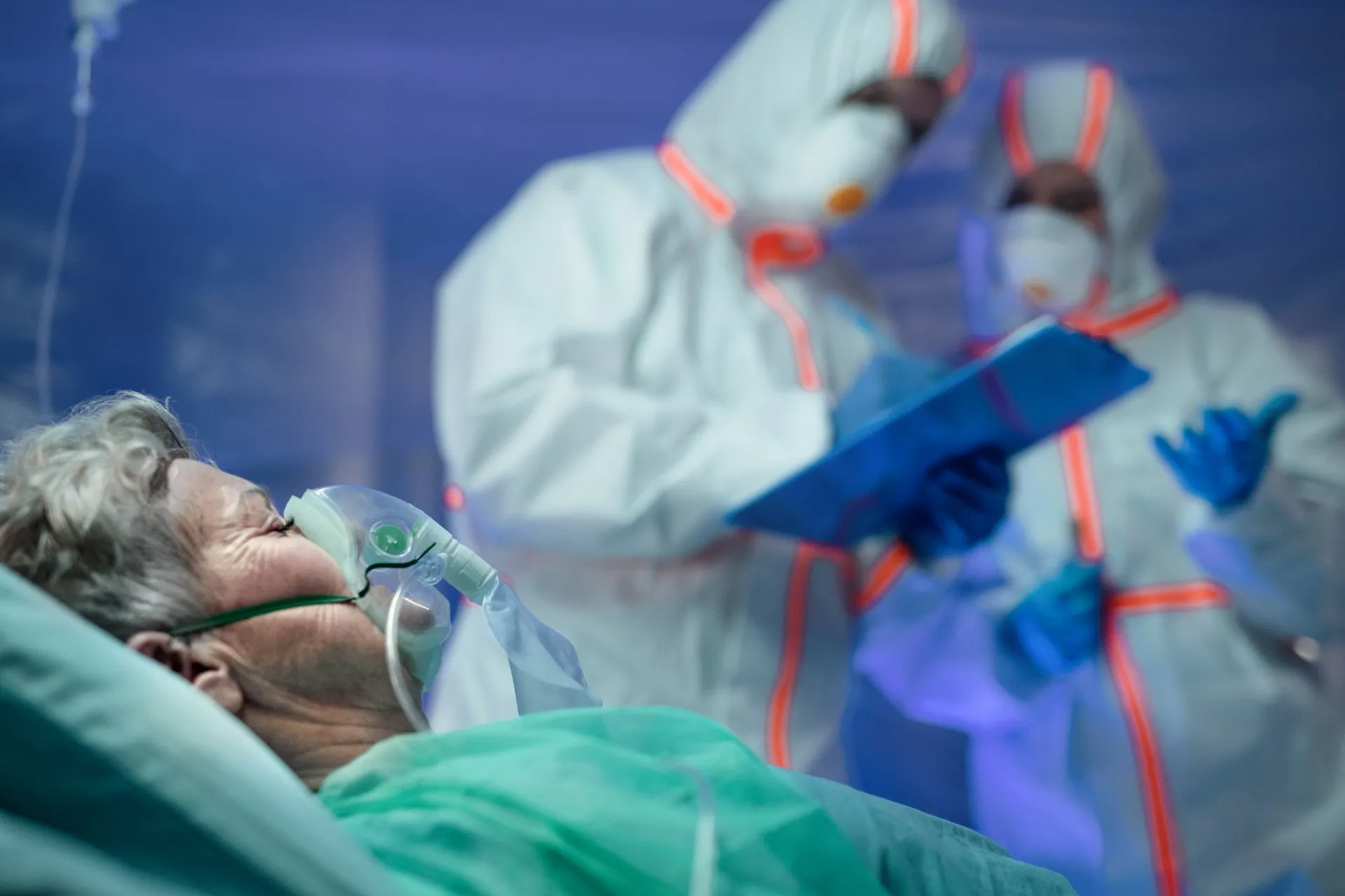 Doctors in hazmat suits discuss patient who lies in hospital bed in foreground - Good Samaritan Society