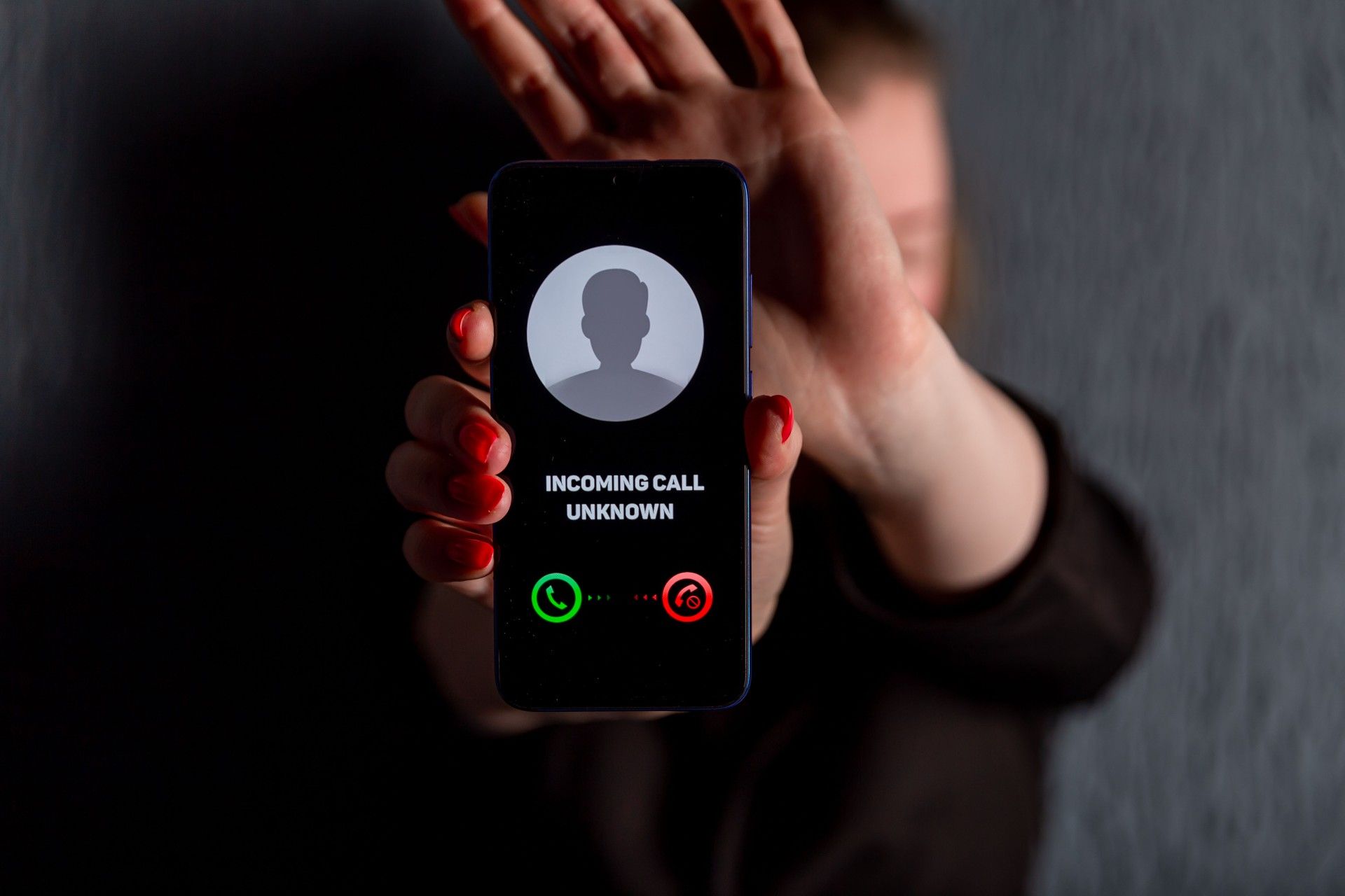 Woman holds out smartphone showing incoming call from an unknown caller as she hides her face - dell