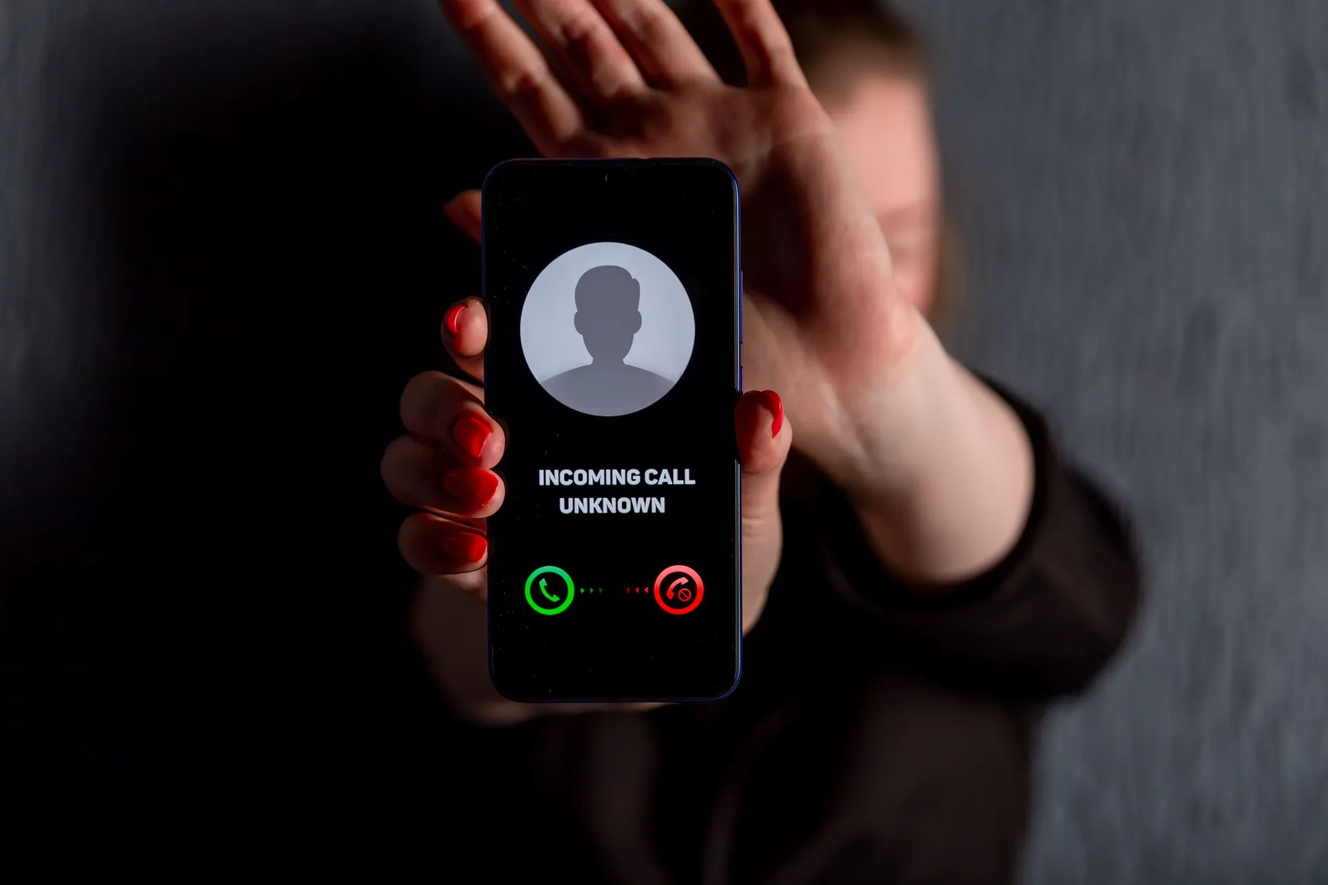 Woman holds out smartphone showing incoming call from an unknown caller as she hides her face - dell