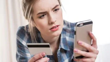 A woman looks concerned while trying to make a payment using a credit card on her smartphone - amex prepaid