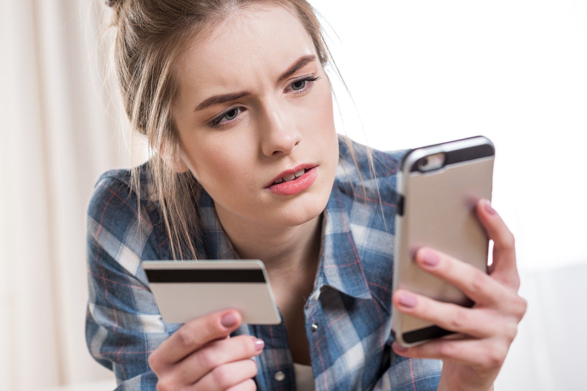 A woman looks concerned while trying to make a payment using a credit card on her smartphone - amex prepaid