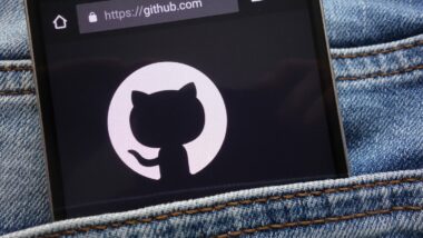 A smartphone with GitHub on the screen sticks out of a pocket on bluejeans