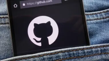 A smartphone with GitHub on the screen sticks out of a pocket on bluejeans