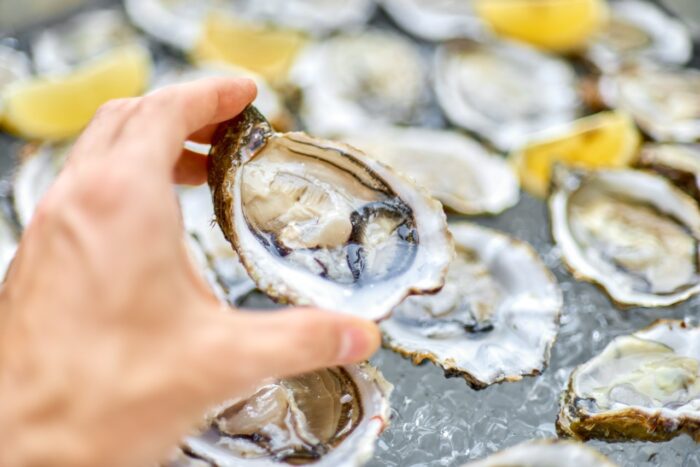 Open oyster in a man's hand, against a background of open oysters, close-up.