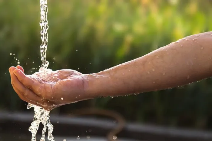 A child cups a small stream of slow flowing water from a single tap - first nations settlement, water class action lawsuit