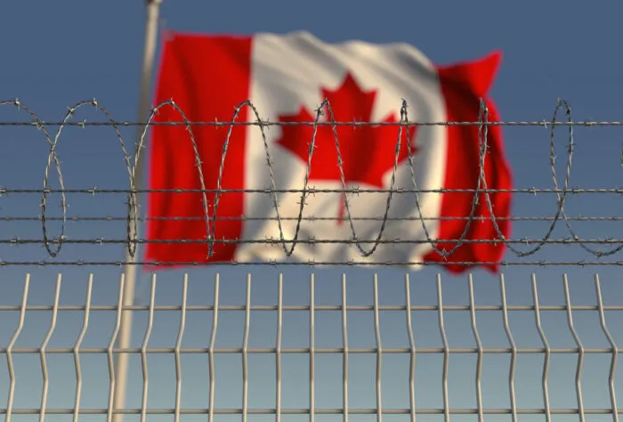 A Canada flag waving in the wind behind a prison fence.