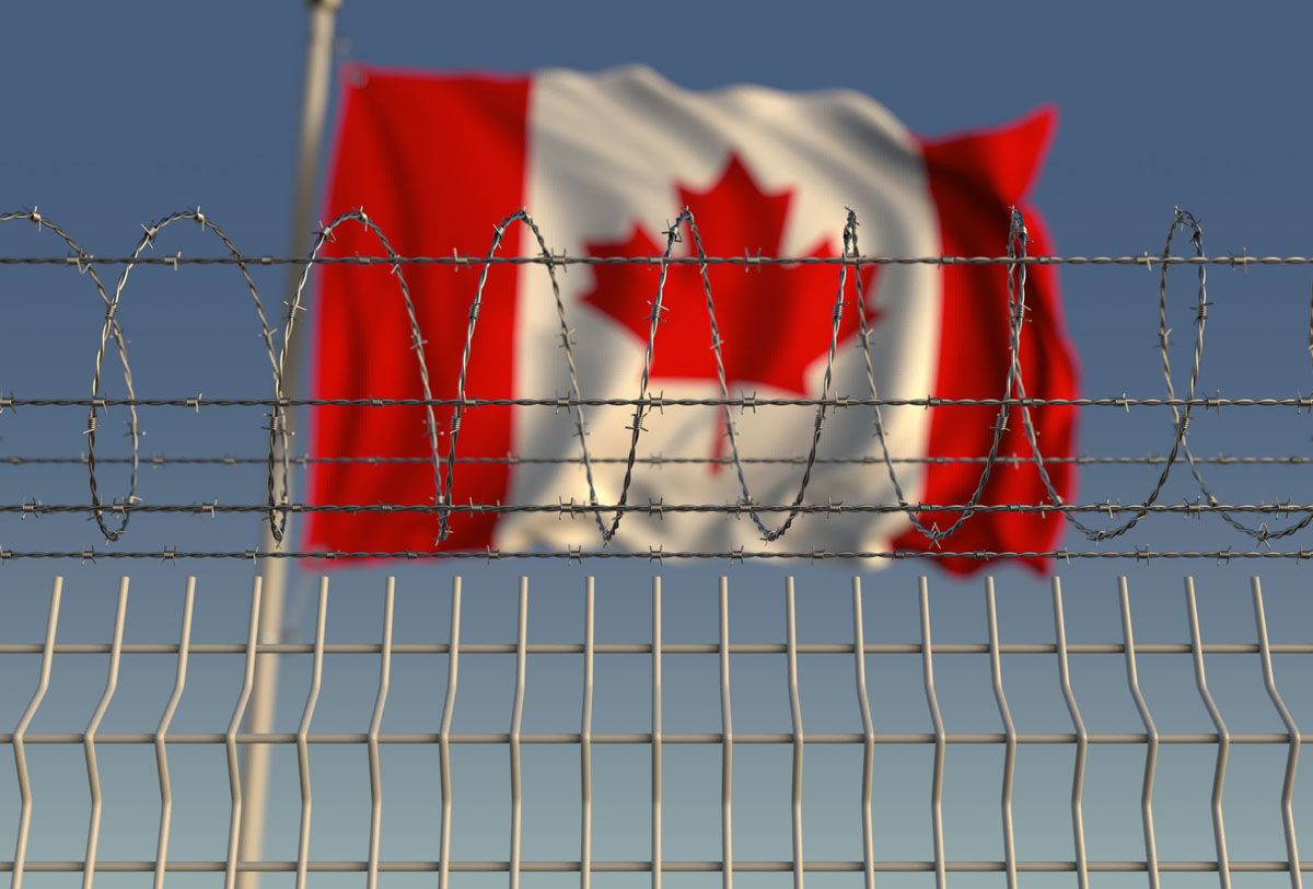 A Canada flag waving in the wind behind a prison fence.