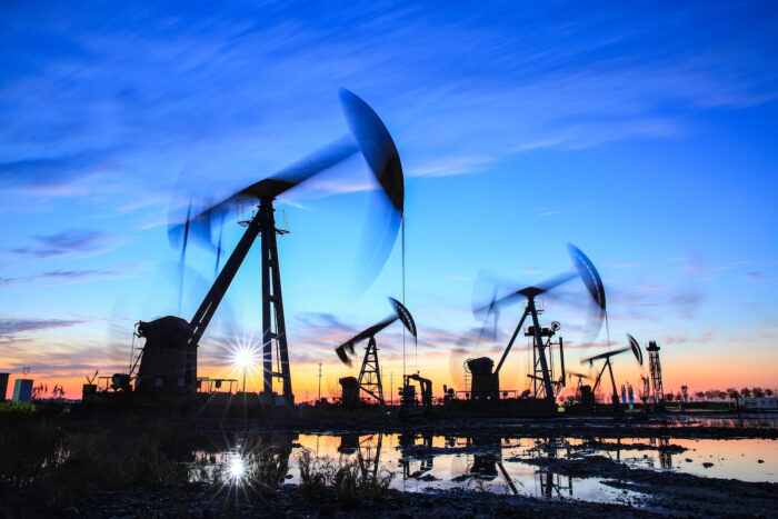 Oil field site, in the evening, oil pumps are running, The oil pump and the beautiful sunset reflected in the water, the silhouette of the beam pumping unit in the evening.