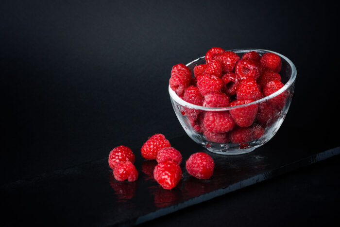 Fresh raspberries in a ceramic bowl isolated on a black background.