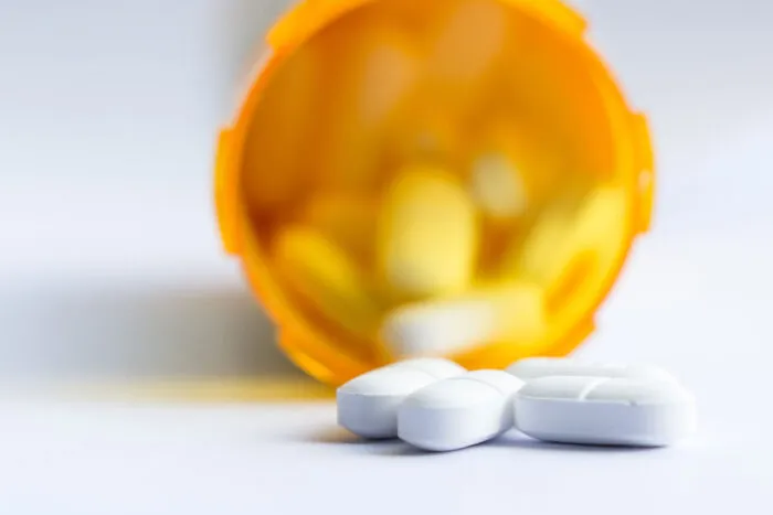 Close up of a group of white tablets with an out of focus prescription bottle in the background.