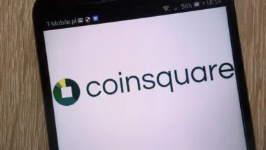 Coinsquare logo displayed on a modern smartphone against a wooden background.