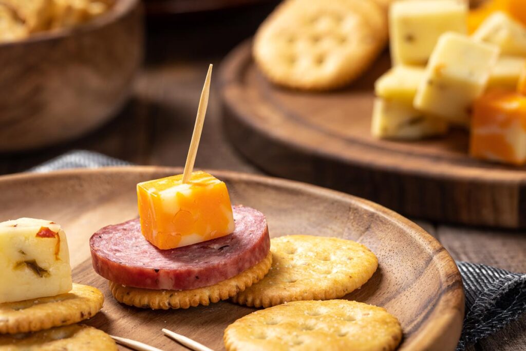 Closeup of sliced salami, cheese cubes and crackers on a wooden plate.