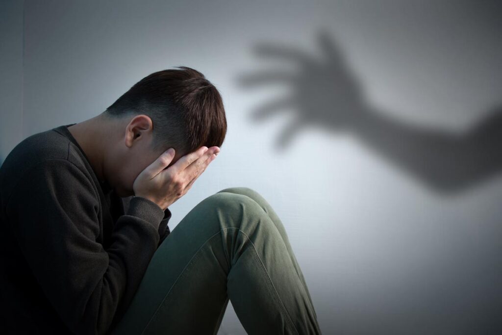A young male crying into his hands with a shadow of a hand reaching out towards him, representing the Newfoundland sexual abuse settlement.