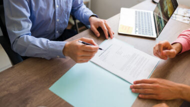 Man pointing to another man where to sign documents, representing the Athletic Trust of Canada timeshare settlement.