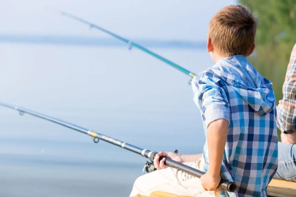 Boy in blue shirt sit on a pier with a fishing rod by the sea