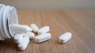 Close up of white pills spilling out of a pill bottle, representing the OxyContin settlement.