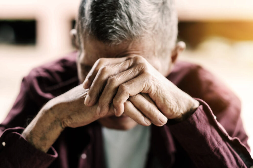 A sad senior man covering his face, representing the Manitoba Developmental Centre abuse settlement.