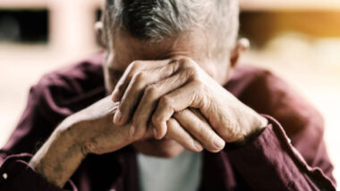 A sad senior man covering his face, representing the Manitoba Developmental Centre abuse settlement.