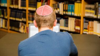 Back view of a male wearing a yarmulke studying on his laptop, representing the anti-semitic universities class action.