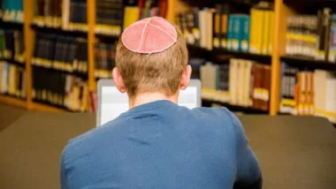Back view of a male wearing a yarmulke studying on his laptop, representing the anti-semitic universities class action.