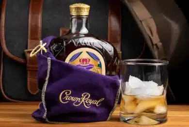 A bottle of Seagram's Crown Royal Canadian rye whiskey in the iconic purple gift bag with a shot in a glass of full of ice cubes.