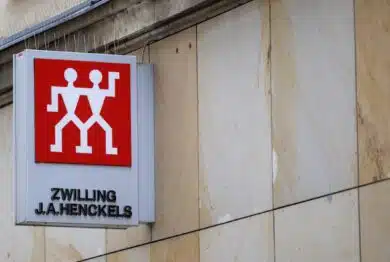 Zwilling J.A. Henckels storefront sign with the red twin figures logo is mounted on a stone building facade in an urban setting.