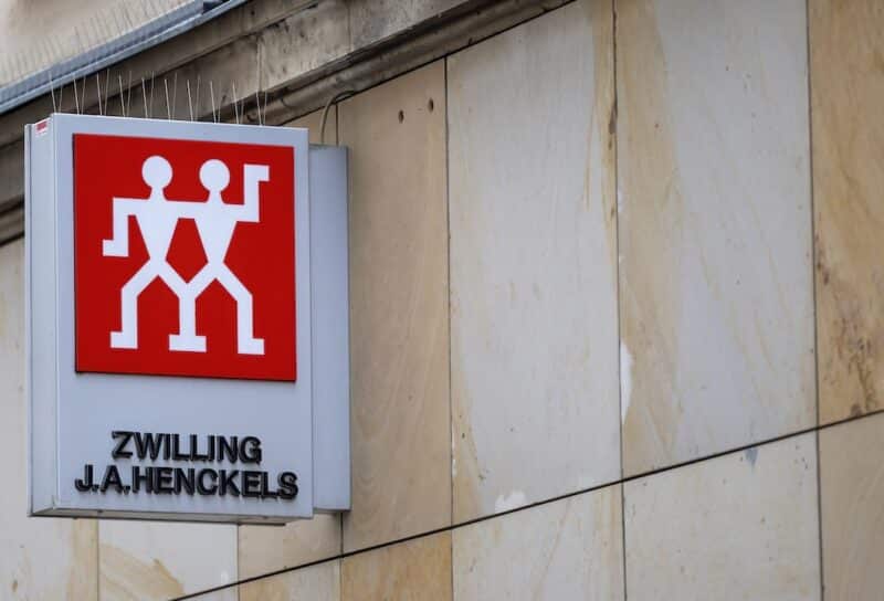 Zwilling J.A. Henckels storefront sign with the red twin figures logo is mounted on a stone building facade in an urban setting.
